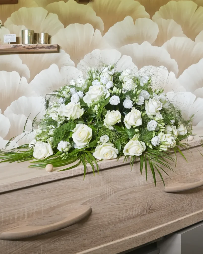 Houten uitvaartkist met een bloemstuk van witte rozen